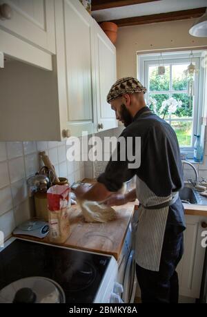 Junger Mann, der Teig auf Küchenoberfläche knetet Stockfoto