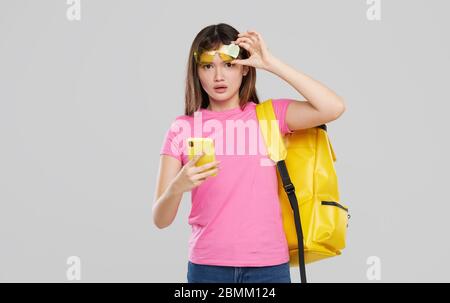 Ein asiatisches Teenager-Mädchen in herzförmiger Brille hält ein Mobiltelefon in den Händen auf grauem Hintergrund. Neue Gadget-Werbung Stockfoto