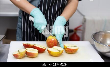 Frau in Gummihandschuhen schneidet Äpfel für die Zubereitung gesunder Lebensmittel Stockfoto