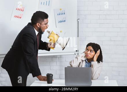 Wütender Boss mit Lautsprecher schreit weibliche Untergebene im Büro an Stockfoto