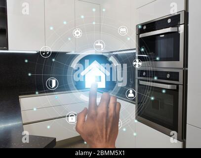 Intelligente Technologien. Millennial Kerl mit modernen Home Control-System in der Küche, Collage mit Symbolen auf virtuellen Bildschirm Stockfoto