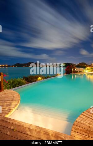 Ein Hotelpool mit Blick auf das Karibische Meer in einer Vollmondnacht in Antigua. Stockfoto