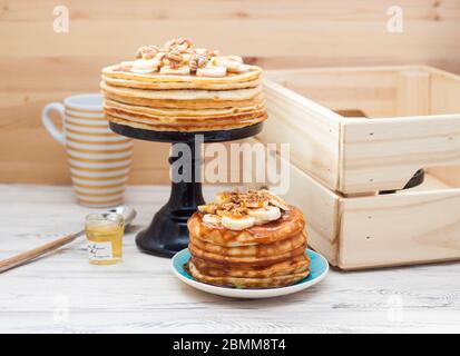 Stapel von flauschigen Pfannkuchen mit Ahornsirup, Banane, Marmelade und Nüsse. Rustikaler Holzhintergrund. Tasse Kaffee. Stockfoto