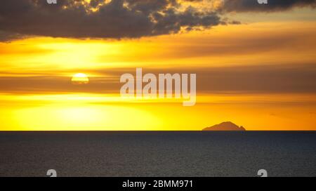 Die Insel Redonda, die zu Antigua & Barbuda gehört, mit einem gelben Sonnenuntergang, der durch die Aschespur des Montserrat-Vulkans erzeugt wird. Stockfoto