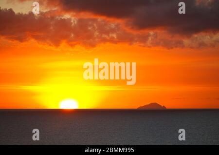 Die Insel Redonda, die zu Antigua & Barbuda gehört, mit einem roten Sonnenuntergang, der durch die Aschespur des Montserrat-Vulkans erzeugt wird. Stockfoto