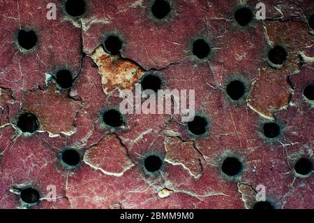 Roter Metallhintergrund mit schwarzen Löchern, Rost und Abrieb. Alte Eisentür in der Garage. Kopierbereich. Stockfoto