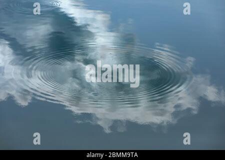 Reflexion der Wolke und blauen Himmel auf Spiegel glattes Wasser. Konzentrische Kreise definieren die Oberfläche des Wassers Stockfoto