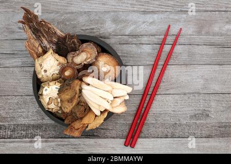 Chinesische Kräuter in der traditionellen alten Kräutermedizin mit roten Essstäbchen auf rustikalem Holzhintergrund verwendet. Stockfoto