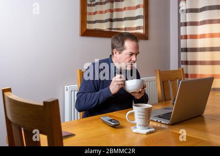 Arbeiten von zu Hause aus, während Frühstück und Kaffee trinken während der COVID 19 Pandemie, Covid-19 Stockfoto