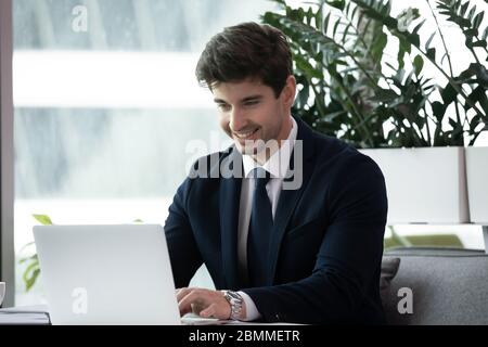 Selbstbewusster Geschäftsmann, der am Schreibtisch sitzt und mit einem Laptop arbeitet Stockfoto