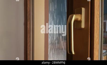 Geschlossenes braunes Kunststofffenster im Haus. Nahaufnahme eines Stiftes. Laminierung von Fenster Glasfolie, ein Paket aus Holz hellbraun. Stockfoto