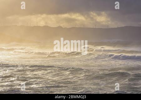 An der Küste brechen große Wellen, im sonnendurchfluteten Meer, die bei Sonnenuntergang durch die Wolken ziehen. Galicien, Spanien. Stockfoto