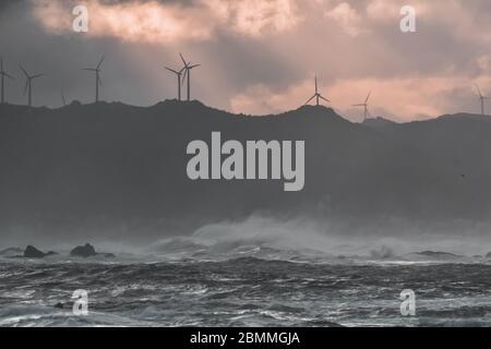 An der Küste brechen große Wellen, im sonnendurchfluteten Meer, die bei Sonnenuntergang durch die Wolken ziehen. Galicien, Spanien. Stockfoto