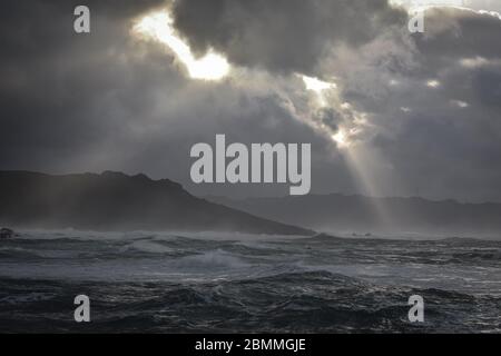 An der Küste brechen große Wellen, im sonnendurchfluteten Meer, die bei Sonnenuntergang durch die Wolken ziehen. Galicien, Spanien. Stockfoto