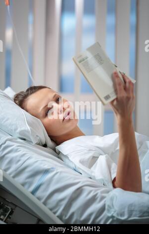 Hübsche, junge, weibliche Patientin in einem modernen Krankenhauszimmer. Neueding eines Buches (flaches DOF; farbgetöntes Bild) Stockfoto