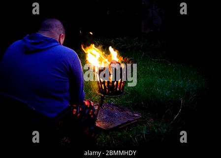 Mann sitzt im Hinterhof vor Feuer im Dunkeln Stockfoto