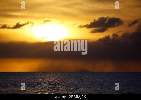 Die Insel Redonda, die zu Antigua & Barbuda gehört, mit einem gelben Sonnenuntergang, der durch die Aschespur des Montserrat-Vulkans erzeugt wird. Stockfoto