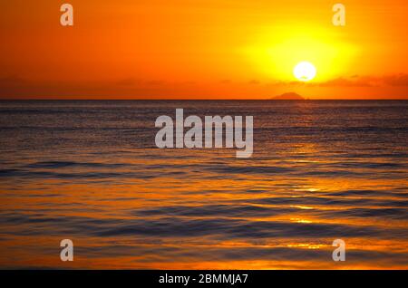 Die Insel Redonda, die zu Antigua & Barbuda gehört, mit einem roten Sonnenuntergang, der durch die Aschespur des Montserrat-Vulkans erzeugt wird. Stockfoto