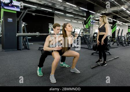 Attraktive Frau und schöner muskulöser Mann Trainer trainieren mit Langhanteln in einem hellen modernen Fitnessstudio. Schönes Mädchen beim Training beobachten Stockfoto