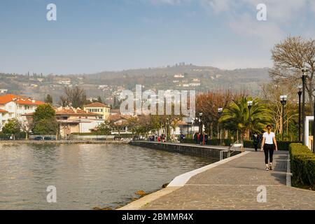 Blick auf die Seepromenade in der Altstadt von Bardolino am Ufer des Gardasees mit Menschen, die an einem sonnigen Wintertag in Venetien, Italien, spazieren Stockfoto