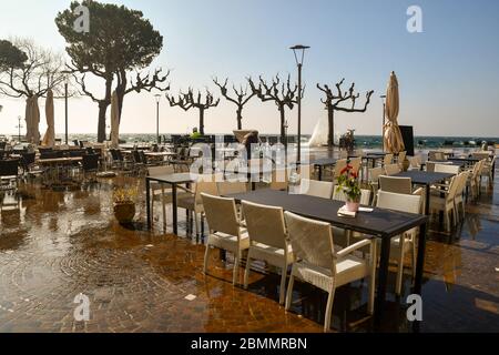 Blick auf das Seeufer mit leerem Outdoor-Café an einem windigen Tag mit hohen Wellen überflutet den See, Garda, Verona, Veneto, Italien Stockfoto