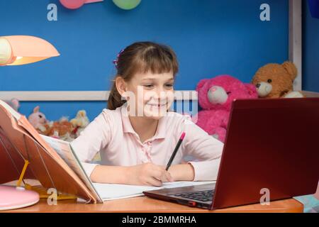 Lächelndes Mädchen am Tisch zu Hause, das in der Schule studiert. Stockfoto