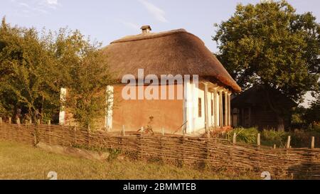 Altes osteuropäisches Landhaus aus Holz mit Wasserzaun und Strohdach. Stockfoto