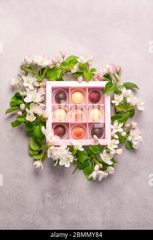 Pralinen in verschiedenen Farben in einer festlichen eleganten Box Verpackung auf einem grauen Hintergrund Dekoration von frischen Blumen. Stockfoto