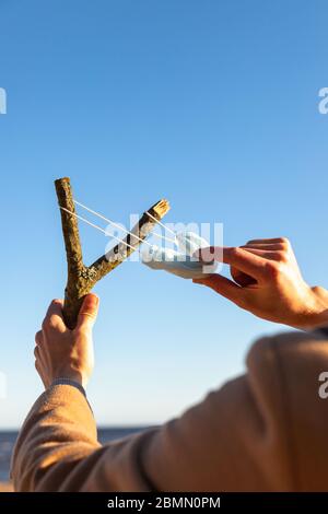 Der Mensch verwendet eine schützende medizinische Maske als Schleuder aus dem Ast, blauer Himmel auf Hintergrund, selektiver Fokus. Genießt das Leben, zurück zum normalen Leben nach CO Stockfoto