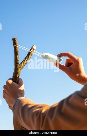 Der Mensch verwendet eine schützende medizinische Maske als Schleuder aus dem Ast, blauer Himmel auf Hintergrund, selektiver Fokus. Genießt das Leben, zurück zum normalen Leben nach CO Stockfoto