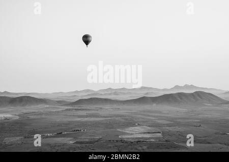 Schwarz-Weiß-Bild im Retro-Stil von einem Heißluftballon über marokko. Schönes Atlasgebirge in der Ferne, mit einem weiteren Ballon am Himmel. Stockfoto