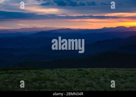 Die Sonne geht hinter den Bergschichten und dem Grasfeld in den Blue Ridge Bergen unter Stockfoto