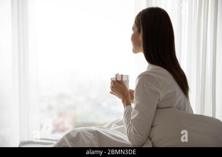 Die Frau wachte auf und saß auf dem Bett und hielt eine Tasse Tee Stockfoto