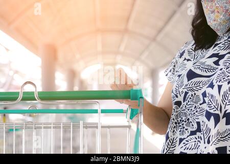 Frau tragen Maske mit Spritzen Alkohol antiseptische Desinfektionsmittel Spray Reinigung auf Warenkorb Trolley Griff Schutz während Coronavirus Pandemie C Stockfoto