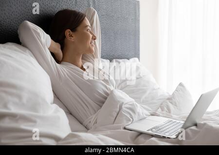 Frau im Bett liegt abgelenkt von Laptop-Nutzung sieht weg Stockfoto