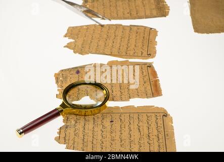 Buchseiten mit einer arabischen Handschrift auf einem Tisch mit einer Lampe und einer Lupe. Paläographie, das Studium der alten arabischen Schrift Stockfoto