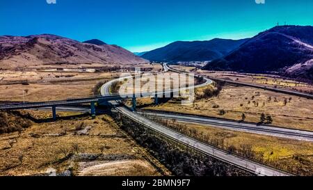 Luftaufnahme einer Autobahnkreuzung in einer ländlichen und bergigen Gegend. Wir sind tagsüber und die Straße ist nicht sehr voll. Stockfoto