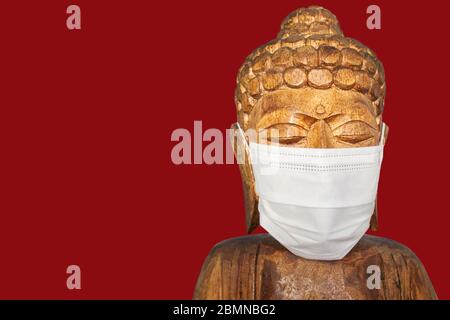 Buddha Holzstatue trägt Gesichtsmaske. Isoliert über rot. Covid-19-Konzept Stockfoto