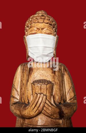 Buddha Holzstatue trägt Gesichtsmaske. Isoliert über rot. Covid-19-Konzept Stockfoto