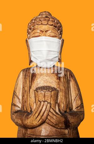 Buddha Holzstatue trägt Gesichtsmaske. Isoliert über gelb. Covid-19-Konzept Stockfoto