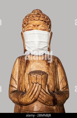 Buddha Holzstatue trägt Gesichtsmaske. Isoliert über Grau. Covid-19-Konzept Stockfoto