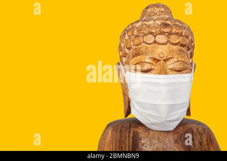 Buddha Holzstatue trägt Gesichtsmaske. Isoliert über gelb. Covid-19-Konzept Stockfoto