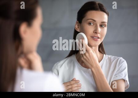 Frau im Spiegel reflektierend hält Gesichtsschwamm reinigt Gesicht Stockfoto