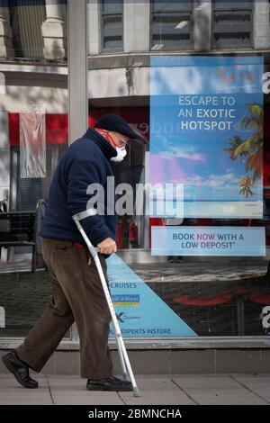 Ein älterer Mann auf Krücken und mit einer chirurgischen Gesichtsmaske geht an einem TUI Reisebüro in Cardiff, Wales, Großbritannien vorbei Stockfoto