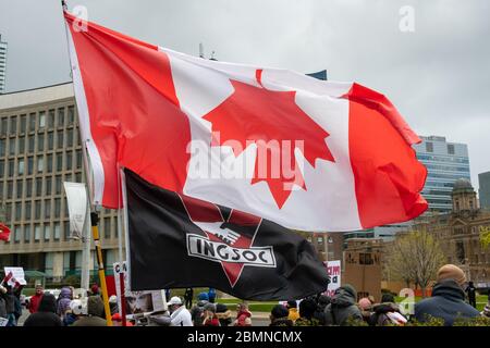 Eine INGSOC-Flagge von George Orwells 1984 fliegt bei einem Protest gegen den COVID-19 Shutdown neben einer umgekehrten Kanada-Flagge vor dem Queen's Park. Stockfoto