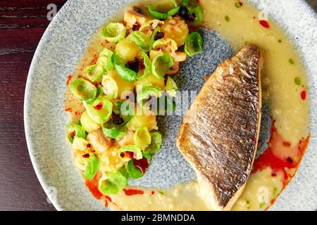 Schmackhaftes gegrilltes Seebarsch-Filet mit gedünsteten rosenkohl, gerösteten Pilzen, Kartoffeln, karamellisierten Zwiebeln und cremiger Sauce, gesundes Abendessen. Oben Stockfoto