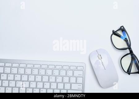 Arbeitsplatz mit Tastatur, Maus und Brille auf einem weißen Tisch mit Kopierfläche und Draufsicht. Nahaufnahme. Stockfoto