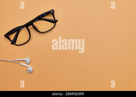 Brille mit Kopfhörern auf orangefarbenem Hintergrund mit Kopierfläche. Draufsicht. Stockfoto