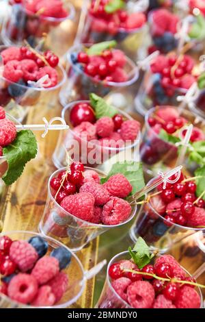 Frische Beeren in Plastikbechern zum Verkauf oder Buffet auf Holztisch angeordnet. Stockfoto