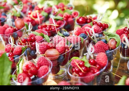 Frische Beeren in Plastikbechern zum Verkauf oder Buffet auf Holztisch angeordnet. Stockfoto
